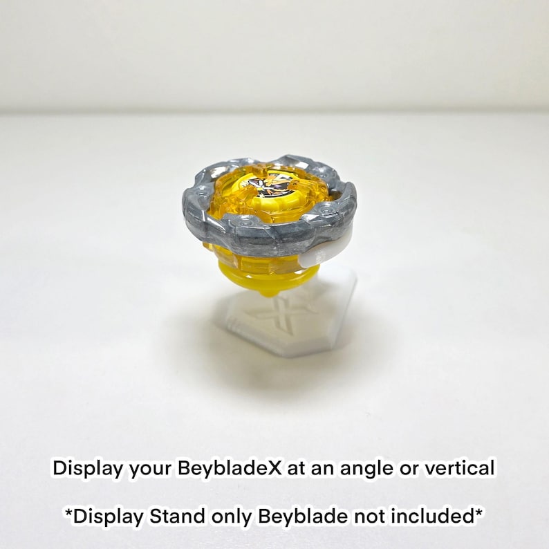 May include: A yellow and grey Beyblade toy on a white display stand. The Beyblade has a yellow centre with a grey outer ring. The display stand is white and has a cross design. Text on the image reads: Display your BeybladeX at an angle or vertical.