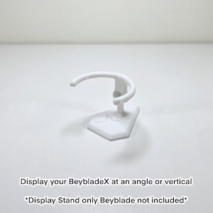 May include: A white display stand for BeybladeX toys. The stand features a curved top and a geometric base. Text on the image reads: "Display your BeybladeX at an angle or vertical. *Display Stand only Beyblade not included*"