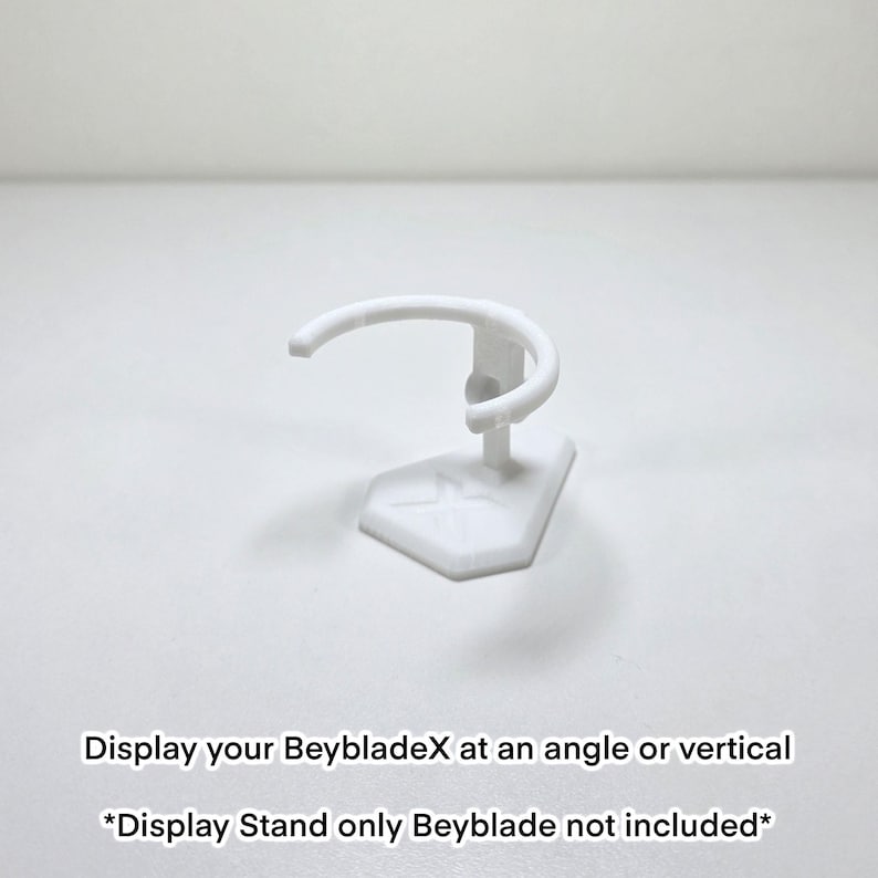 May include: A white display stand for BeybladeX toys. The stand features a curved top and a geometric base. Text on the image reads: "Display your BeybladeX at an angle or vertical. *Display Stand only Beyblade not included*"
