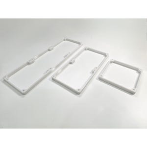 May include: Three white rectangular frames of varying lengths, each featuring a raised border and small circular mounting holes at the corners and along the sides. The frames are constructed with a visible layered texture and open centers.