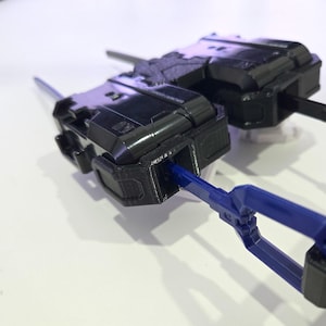 Pu&ograve; includere: Un dispositivo di lancio meccanico in plastica nera caratterizzato da un alloggiamento rettangolare con superfici testurizzate e un meccanismo a strappo in plastica blu che si estende lateralmente. Il dispositivo presenta dettagli stampati.