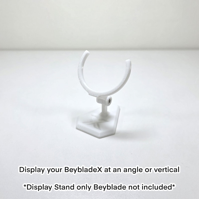 May include: A white display stand for BeybladeX toys. The stand features a curved top and a hexagonal base. The image text says: "Display your BeybladeX at an angle or vertical. *Display Stand only Beyblade not included*"