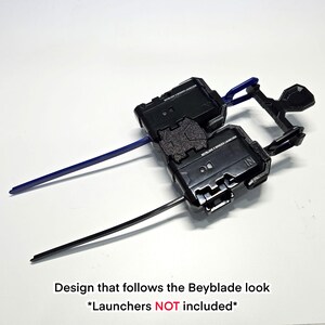 Pu&ograve; includere: Un supporto in plastica nera per lanciatori Beyblade X dal design geometrico. Il supporto presenta due slot per lanciatori e include una striscia di plastica blu e una striscia di plastica nera inserite lateralmente. Il testo BEYBLADE X WINDER LAUNCHER &egrave; stampato sulla superficie.