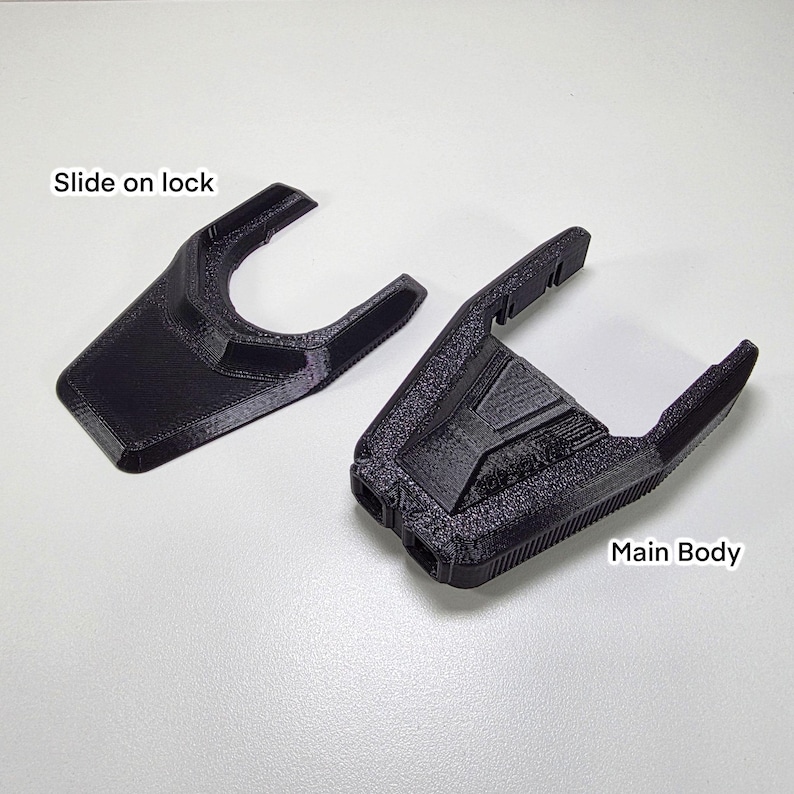 May include: Two black 3D-printed plastic components. One is labeled "Slide on lock" and the other "Main Body". The "Slide on lock" piece has a curved shape. The "Main Body" component has a geometric design with two cylindrical openings.
