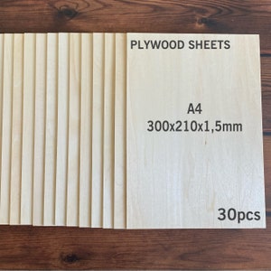 Può includere: Una pila di trenta fogli rettangolari di compensato di colore chiaro. Il foglio superiore riporta il testo stampato PLYWOOD SHEETS, A4, 300x210x1,5mm e 30pcs. Ogni foglio presenta una venatura del legno naturale e liscia color beige.