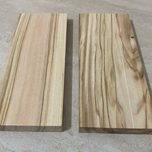 Könnte beinhalten: Zwei rechteckige Holzbretter mit hellbrauner Farbe und sichtbarer Holzmaserung. Die Bretter liegen nebeneinander und zeigen die natürlichen Muster und Texturen des Holzes. Das Holz hat ein glattes, fertiges Aussehen.