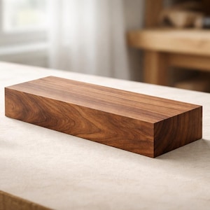 Pode incluir: Um bloco retangular de madeira castanha escura com padrões de grão visíveis. O bloco de madeira é exibido em uma superfície de cor clara, mostrando sua textura natural e variações de cor. O bloco parece recém-cortado.