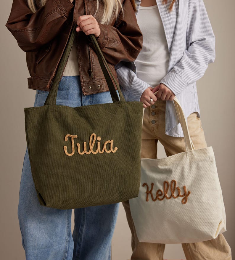 May include: Two corduroy tote bags, one olive green and one cream. The olive green bag has the name "Julia" embroidered in a light brown script. The cream bag has the name "Kelly" embroidered in a light brown script.