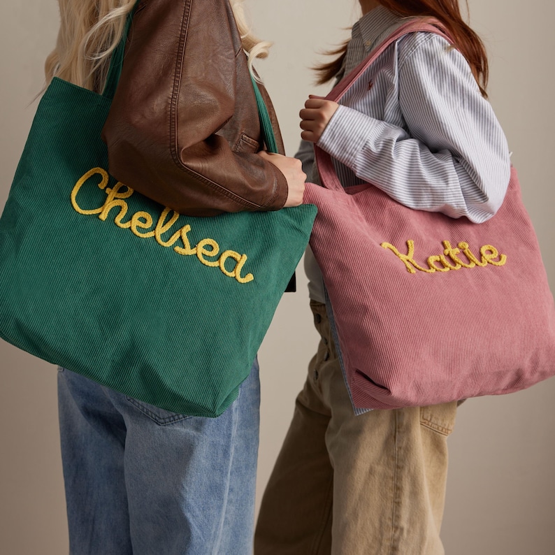 May include: Two corduroy tote bags, one emerald green and one dusty rose, are displayed. The green bag has "Chelsea" embroidered in yellow, while the pink bag has "Katie" embroidered in yellow. Both bags have a simple, rectangular design.