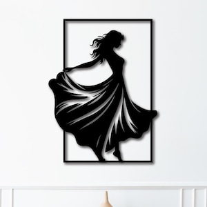 Może przedstawiać: Czarna metalowa grafika ścienna przedstawiająca kobietę w powłóczystej sukni, oprawiona w czarny prostokąt. Grafika jest zamontowana na białej ścianie nad drewnianą szafką z dwiema szufladami i bocznymi drzwiami.