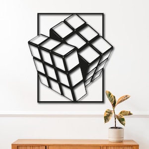 Può includere: Una scultura da parete in metallo nero di un cubo di Rubik 3D, con sfondo bianco. La scultura è montata su una parete bianca sopra una cassettiera in legno e uno sgabello in legno.