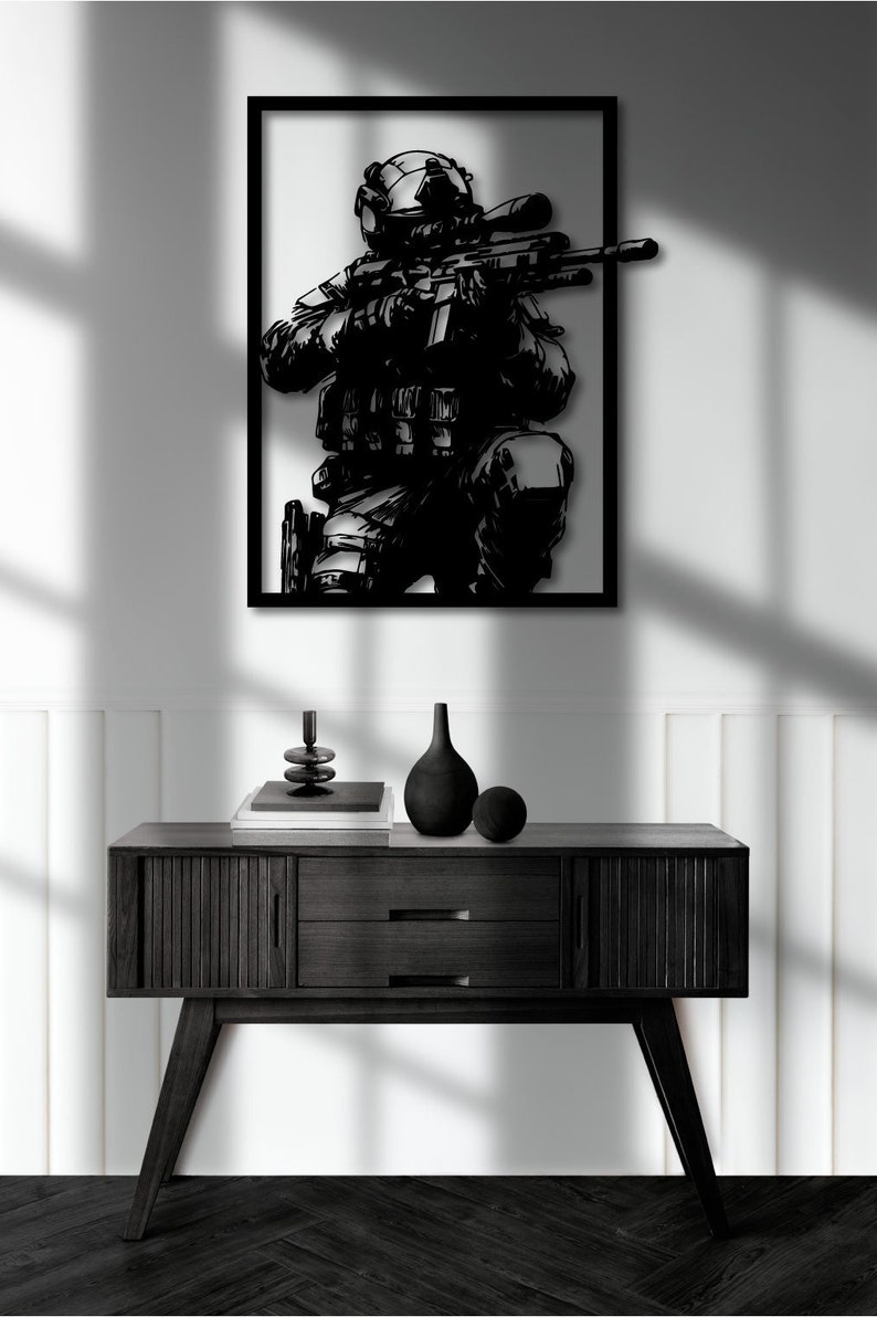 May include: Black and white silhouette of a soldier holding a rifle, framed in a black frame and hanging on a white wall above a black console table.