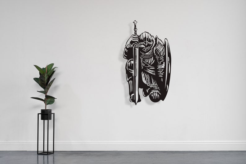 May include: Black metal wall art depicting a kneeling knight holding a sword and shield.
