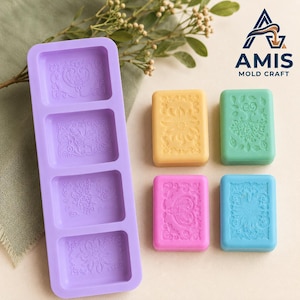 May include: A rectangular purple silicone mould with four distinct cavities, each featuring a unique embossed floral or butterfly pattern. Beside the mould are four small rectangular soap bars in yellow, green, pink, and blue, each displaying a matching embossed design.