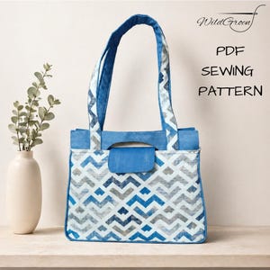 Op de afbeelding: Een draagtas met een blauw, grijs en wit chevronpatroon met effen blauwe accenten op het bovenpaneel, het handvat en de klepsluiting. De tekst WildGroen PDF SEWING PATTERN is zichtbaar in de rechterbovenhoek van de afbeelding.