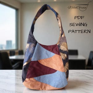 Op de afbeelding: Een patchwork schoudertas met een gebogen ontwerp. De tas heeft een mix van kleuren, waaronder blauw, bordeauxrood en bruin. De tekst "WildGreen" en "PDF SEWING PATTERN" zijn zichtbaar.