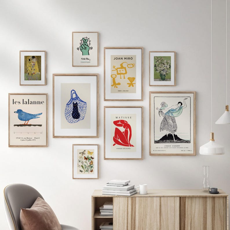May include: A collection of framed art prints in various sizes and styles. The prints include abstract designs, botanical illustrations, and reproductions of famous artworks. The frames are a light brown color, and the prints are displayed on a white wall.
