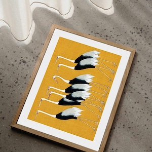 May include: A framed print featuring a flock of cranes in flight. The birds have white and black plumage with long, thin legs and beaks. The background is a solid yellow, and the frame is made of light-colored wood.