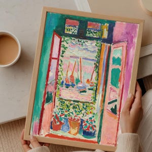 May include: A framed painting with a vibrant, impressionistic style. The artwork depicts a window scene with sailboats, flowers, and lush greenery. The color palette includes pink, green, blue, and orange hues. The artist's signature is visible in the bottom right corner.