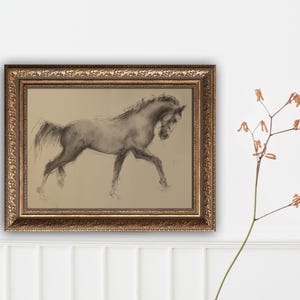 May include: A framed charcoal drawing of a horse in motion. The artwork is in a gold ornate frame. The horse is depicted in shades of gray and black against a tan background. The artwork is displayed on a white wall.