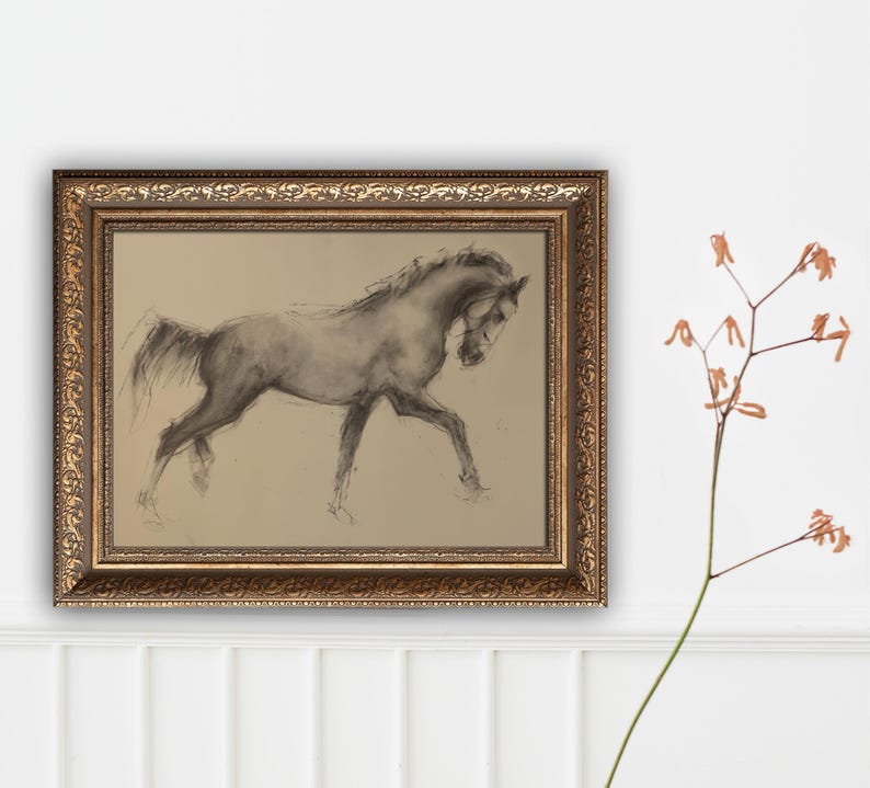 May include: A framed charcoal drawing of a horse in motion. The artwork is in a gold ornate frame. The horse is depicted in shades of gray and black against a tan background. The artwork is displayed on a white wall.