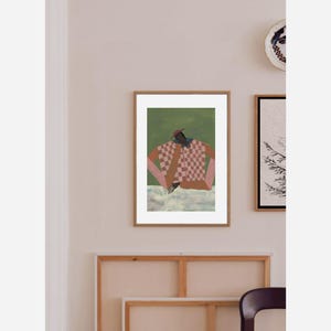 May include: A framed art print featuring a figure in a checkered shirt and a red hat, set against a green backdrop. The artwork has a modern, abstract style with a focus on color and form. The frame is a warm brown.
