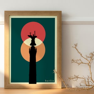 Puede incluir: Una impresión enmarcada con un fondo verde azulado que presenta una silueta negra de una columna con una figura alada en la parte superior. Dos círculos superpuestos, uno rojo y otro naranja, están detrás de la columna. El texto "berlin" está en la parte inferior de la impresión.