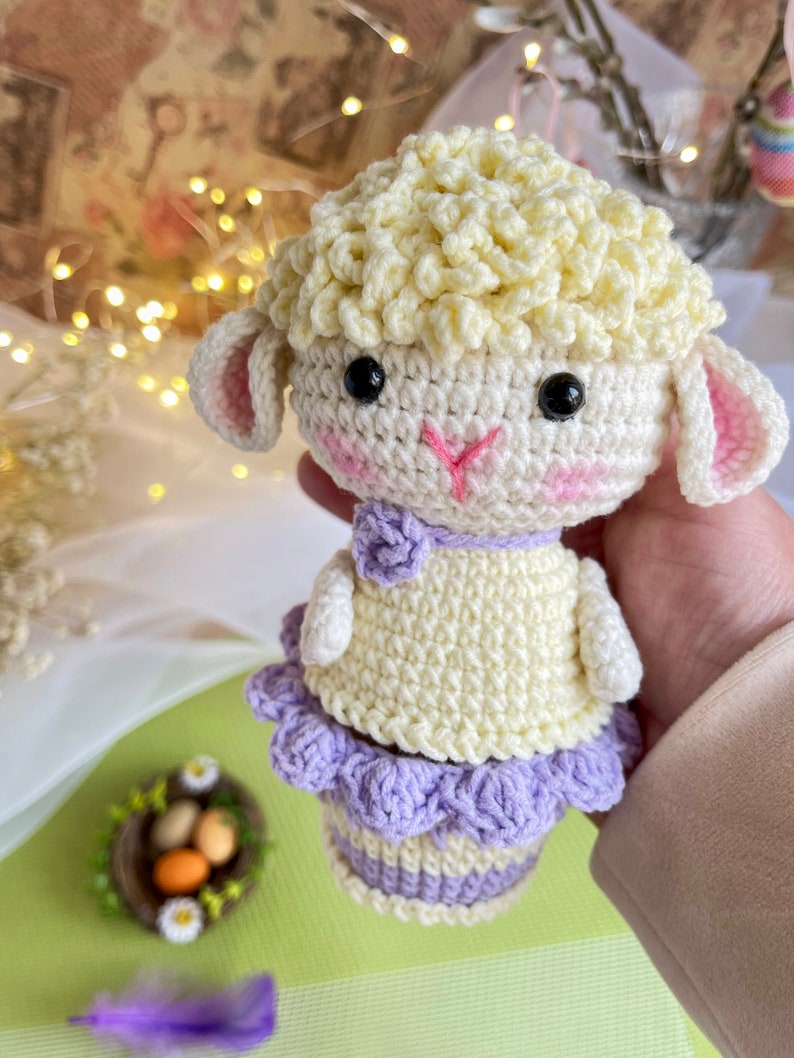 May include: A crocheted Easter lamb with a white body, yellow curly hair, and a purple skirt. The lamb is holding a basket of eggs.