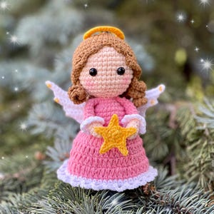May include: A crocheted angel doll with brown hair, a pink dress, white wings, and a gold halo. The angel is holding a yellow star.