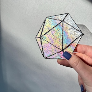 Peut inclure: Un attrape-soleil icosaèdre géométrique fabriqué en verre teinté irisé avec une surface texturée et scintillante. Les panneaux triangulaires individuels sont assemblés par de fines lignes de soudure en métal sombre, créant un objet facetté.
