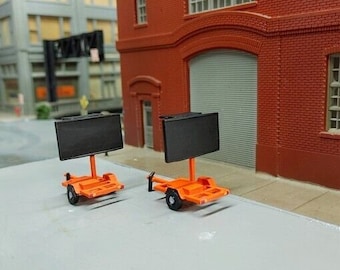 May include: Two orange trailer hitches with black rectangular signs. The trailers are on a gray surface.