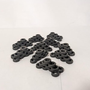May include: A collection of small, dark gray toy tires arranged in various pyramid shapes. The tires have detailed tread patterns and are stacked in groups, creating a playful and miniature automotive theme.