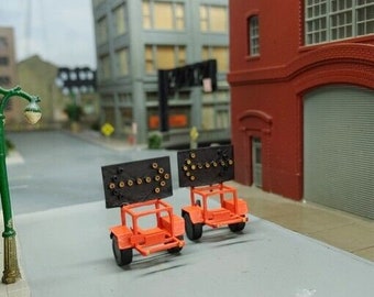 May include: Two orange toy trailers with black arrow signs on the back. The trailers are on a gray surface in front of a brick building.