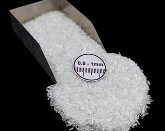 May include: A close-up shot of a pile of small, clear, crystalline particles, possibly a mineral or chemical compound, spilling from a metal scoop. A circular label indicates a size range of 0.5-1mm.