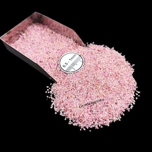 May include: Pink gemstone gravel displayed in a metal scoop. A white circular label with the text "0.5 - 1mm" and a ruler is visible. The background is black. The text "Gradelygems" is in the bottom right corner.