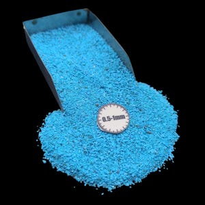 May include: A close-up of a pile of small, bright turquoise stones, possibly crushed turquoise, spilling from a metal scoop. A small white label with the text "0.5-1mm" is visible. The background is black.