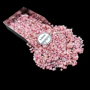 May include: A collection of small, pink gemstones, varying in shade, are presented against a black backdrop. A metal scoop contains some of the stones. A white tag reads "3-5mm". The text "Gradelygems" is also visible.