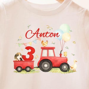 Könnte beinhalten: Weißes T-Shirt mit einem roten Traktor, der einen Wagen mit einem Meerschweinchen zieht. Das Design enthält den Namen "Anton", die Zahl "3", Ballons und Bauernhoftiere. Ein Geburtstagsthema.