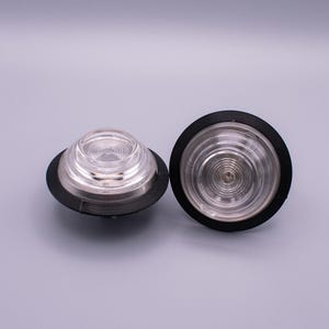May include: Two white LED dome lights with black bezels. The lights have a clear lens with a series of concentric rings.