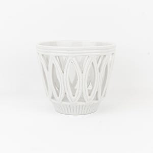 Könnte beinhalten: Ein weißer Keramik-Pflanztopf mit einem durchbrochenen Design. Der Topf hat eine zylindrische Form mit ovalen Aussparungen an den Seiten. Der Boden hat eine gerippte Textur. Misst etwa 15 cm hoch und ist für drinnen oder draußen geeignet.