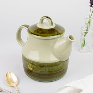 May include: A green and white ceramic teapot with a lid and a handle. The teapot has a brown glaze and a striped pattern.