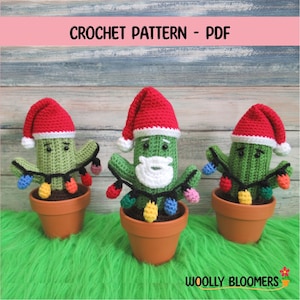 May include: Three crocheted cactus ornaments wearing Santa hats and holding colorful string lights. The cacti are in terracotta pots and are sitting on a green fuzzy surface. The text "WOOLY BLOOMERS" is visible at the bottom of the image.