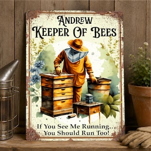 May include: A rectangular metal sign with a distressed border featuring a beekeeper in a yellow suit and protective veil tending to a wooden beehive. The text reads: Andrew Keeper Of Bees. If You See Me Running... You Should Run Too!