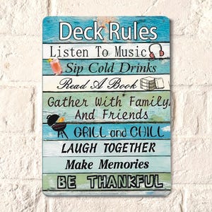 Puede incluir: Un letrero de madera azul y blanco con el texto "Deck Rules" y una lista de reglas para disfrutar del tiempo en una terraza, incluyendo escuchar música, beber bebidas frías, leer un libro, hacer barbacoas y crear recuerdos.