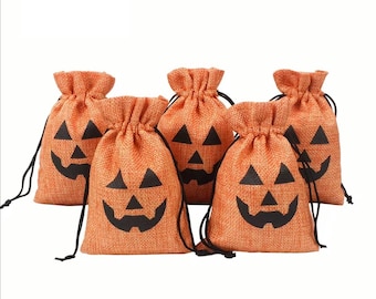 May include: Five orange burlap drawstring bags with black jack-o'-lantern faces. Each bag has a black drawstring closure. The bags are a festive decoration for Halloween.