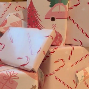 May include: A stack of pink and white gift wrap with various Christmas designs. The designs include candy canes, Christmas trees, and cars with Christmas trees on top. The gift wrap is ideal for wrapping presents for the festive season.