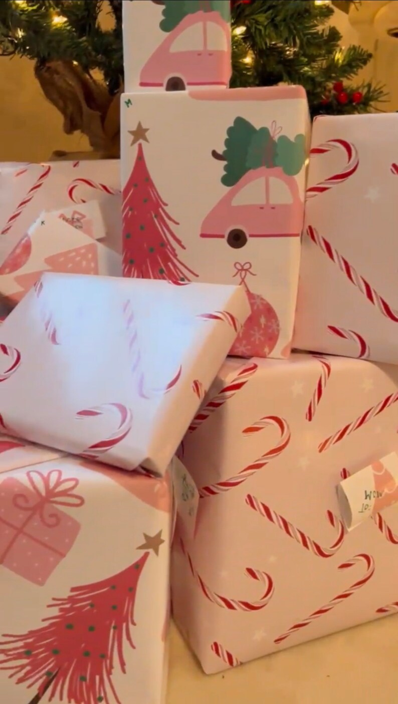 May include: A stack of pink and white gift wrap with various Christmas designs. The designs include candy canes, Christmas trees, and cars with Christmas trees on top. The gift wrap is ideal for wrapping presents for the festive season.