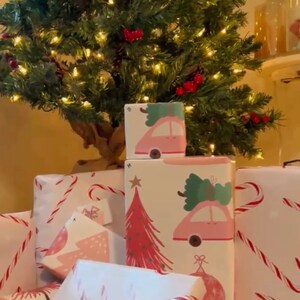 May include: A stack of wrapped Christmas presents with pink and white paper featuring candy canes, Christmas trees, and cars.