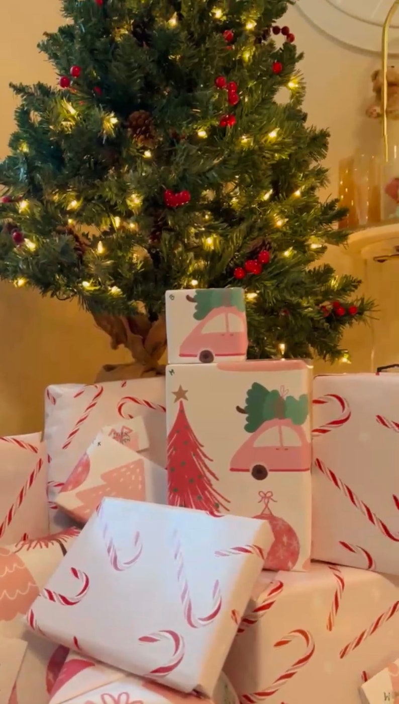 May include: A stack of wrapped Christmas presents with pink and white paper featuring candy canes, Christmas trees, and cars.