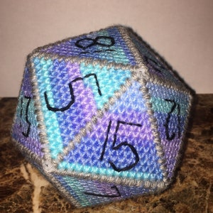 May include: A blue, purple, and gray crocheted dice with numbers 1, 2, 3, 4, 5, 6, 7, 8, 9, 10, 11, 12, 13, 14, and 15.